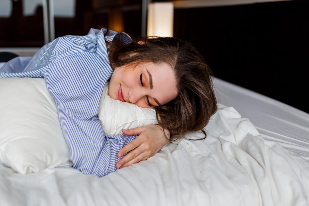A woman peacefully sleeping on a bed with a relaxed smile, enjoying a comfortable and restful night’s sleep.