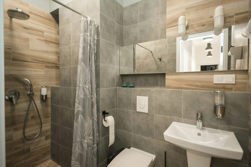 A modern bathroom with neutral tones, featuring wood and gray tiles, a frameless mirror, and a minimalist sink.