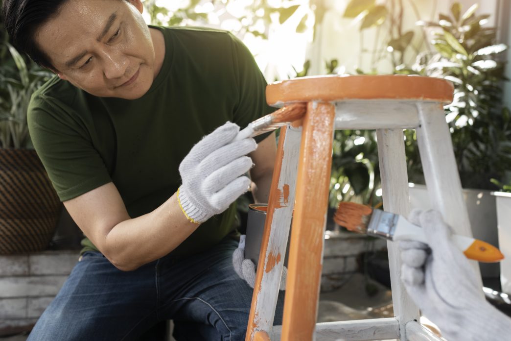 Man painting a wooden chair orange and white as a DIY furniture project.