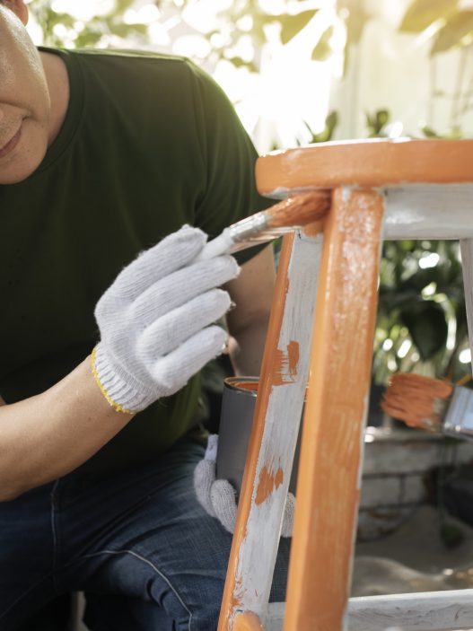 Man painting a wooden chair orange and white as a DIY furniture project.