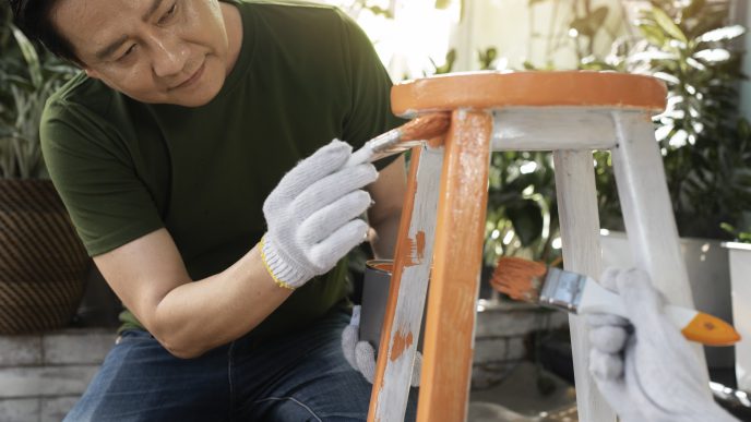 Man painting a wooden chair orange and white as a DIY furniture project.