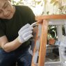 Man painting a wooden chair orange and white as a DIY furniture project.